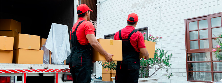 Two men in red hats and overalls are seen carrying boxes, highlighting the importance of hiring dependable Seattle movers.