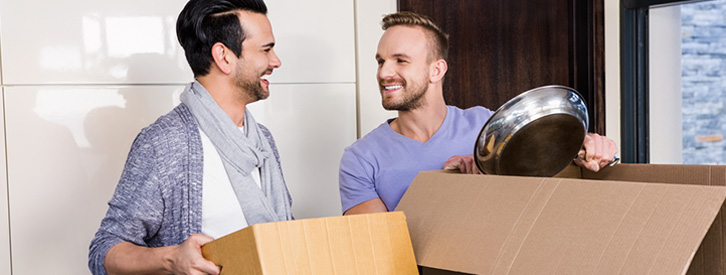 Two guys smiling and carrying moving boxes.