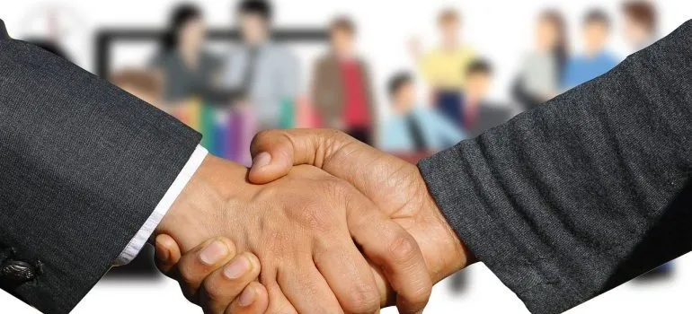 A close up of a handshake with people in the back. 