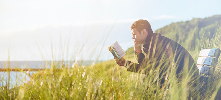 A man reading a book an a bench by some big body of water
