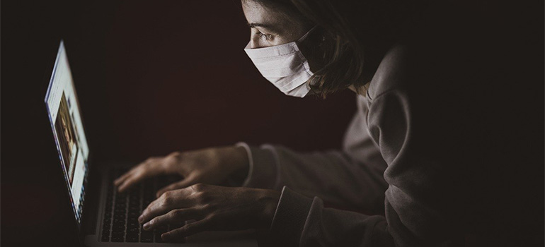 A person with a mask using laptop.
