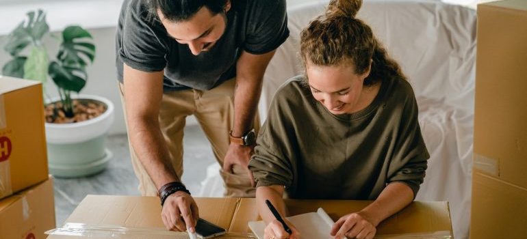 A couple writing in a notebook placed on moving boxes.