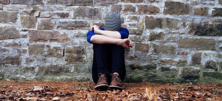 Person sitting alone next to a wall, struggling with overcoming post-moving depression.