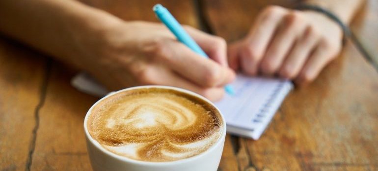 A cup of coffee and a person writing in a notepad in order to give your movers feedback.