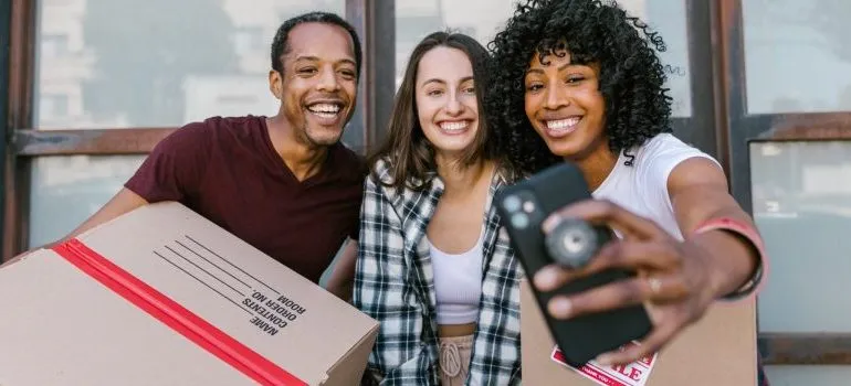 three people carrying moving boxes, taking a selfie 