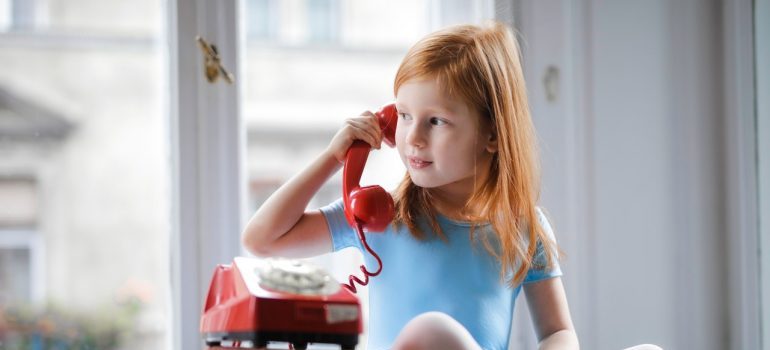 A little girl in a blue dress playing with a red phone