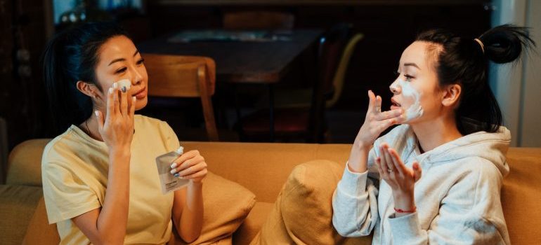 two women sitting on the couch and putting cream on their faces