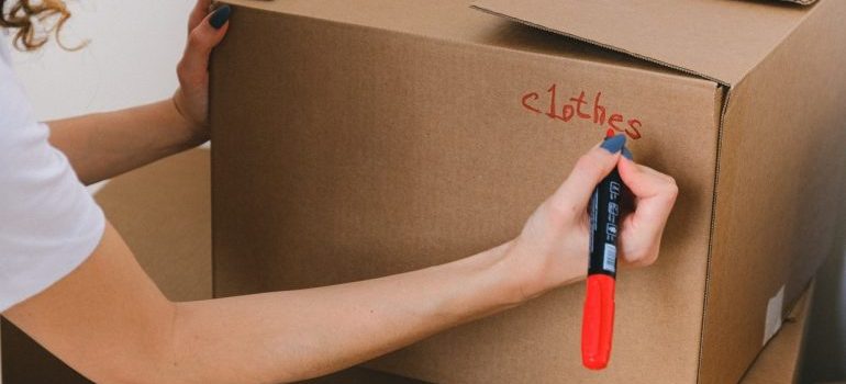 a woman writing the word clothes on the box using the red marker