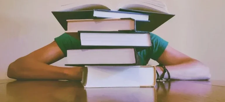 Person hiding behind books and thinking about storing books and photos
