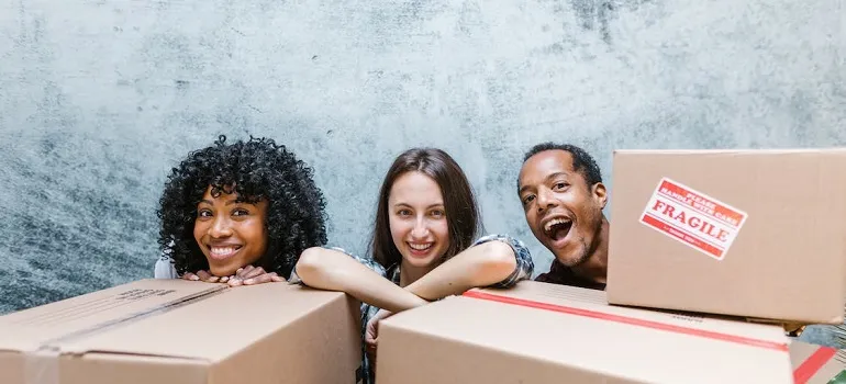 Three people hiding behind moving boxes know the benefits of being a mover and driver