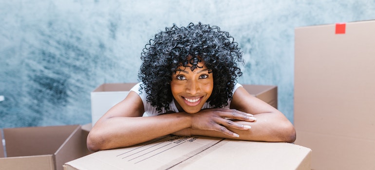 A Woman with Curly Hair Smiling leaning on a moving box
