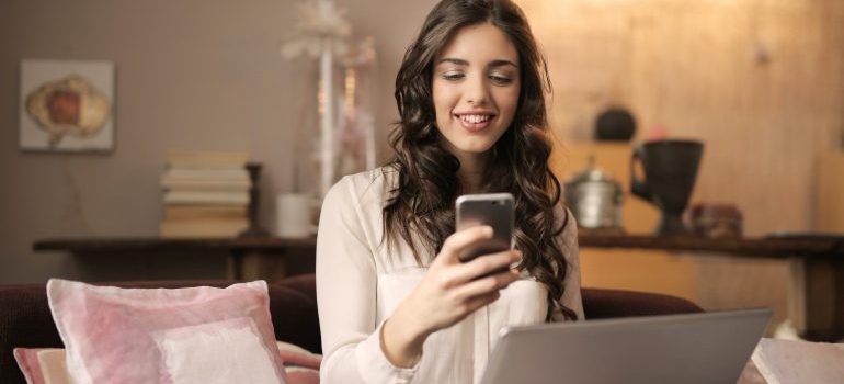 Woman using her phone and laptop in search of things to know about moving company reviews