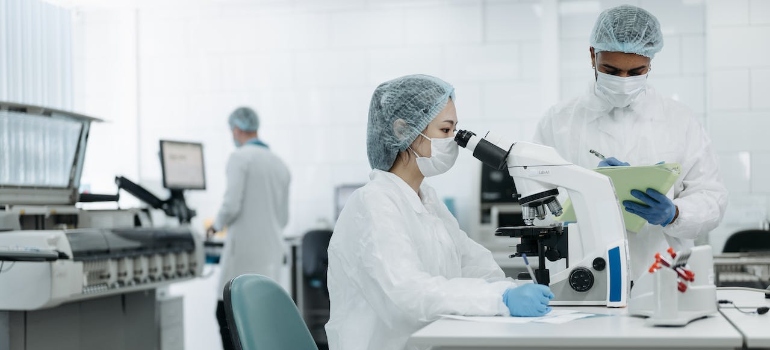 Woman in white protective suit looking through microscope after medical equipment and lab relocation