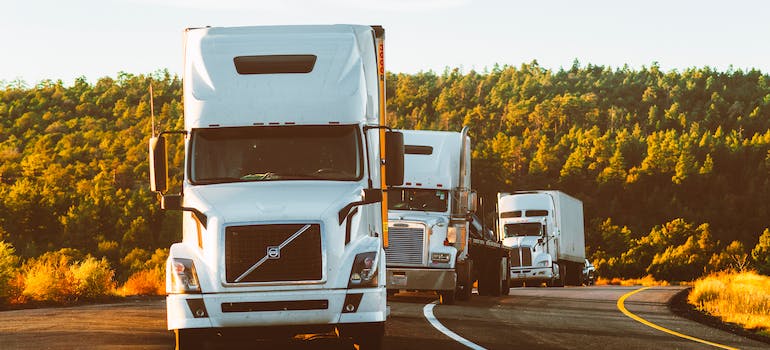 Three white Volvo semi-truck on the side of road