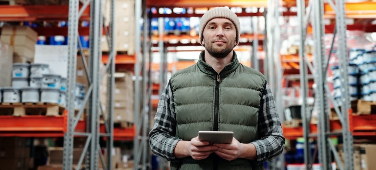 A man in bubble jacket holding tablet computer in a distribution and logistics warehouse
