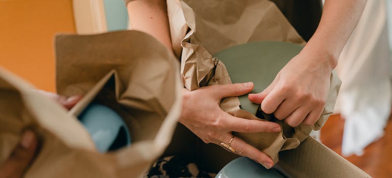 A person packing ceramic tableware in parchment