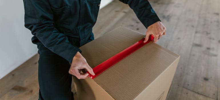 A man sealing a cardboard box with packing tape employing effective packing strategies