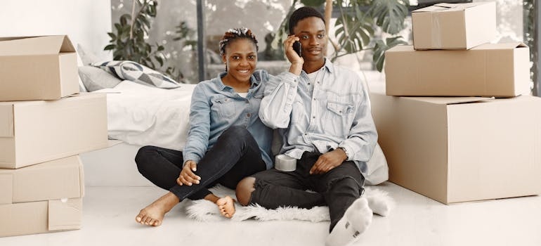 A Couple Sitting beside Cardboard Boxes in a Bedroom
