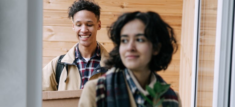 A Woman Wearing a Trench Coat by the Door Followed by a Man Carrying a Box on a moving day in Seattle