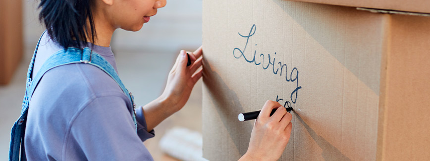 packing for a relocation. Woman writing on a box for better tip moving guide.