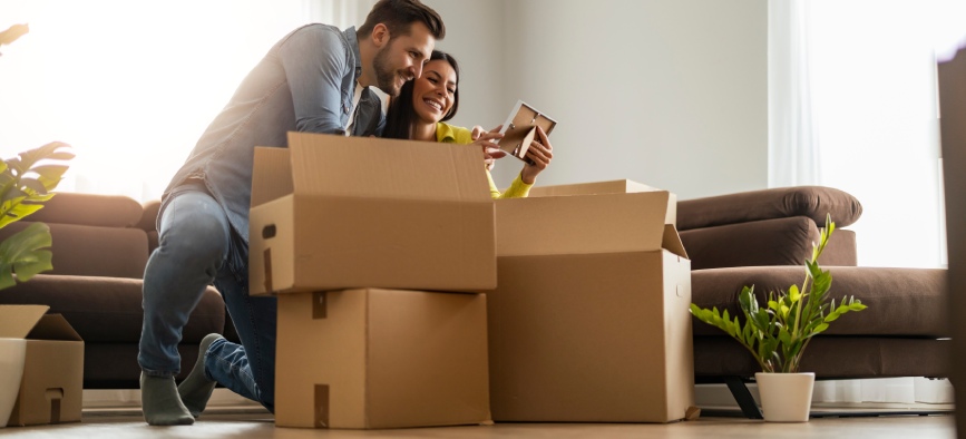 Happy young married couple moves to new apartment and unpaking boxes.