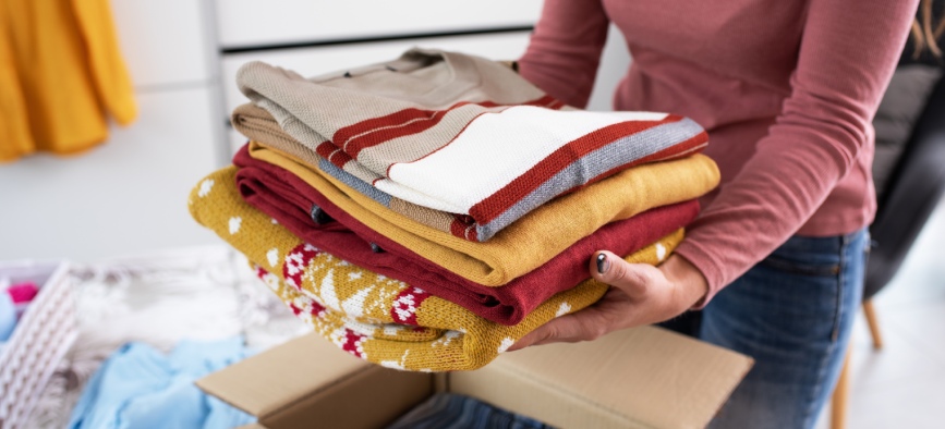 Young woman folding her clothes and packing them in a delivery box, she is changing her wardrobe