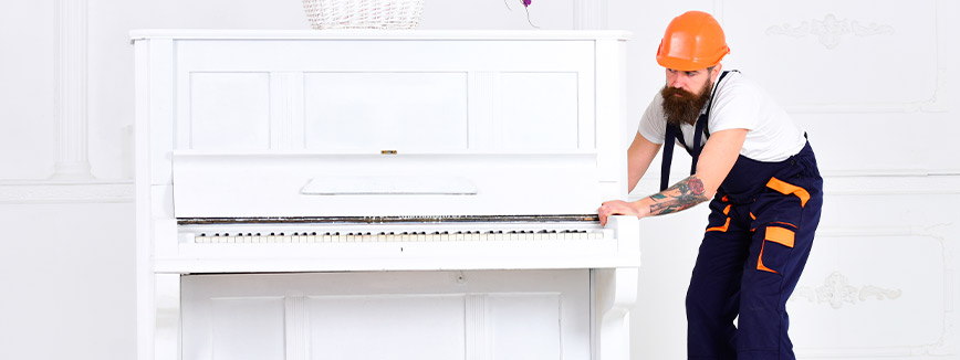 A man in overalls and an orange hat plays an upright piano, showcasing his musical talent and passion for music.